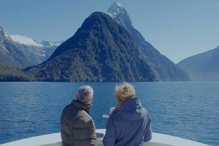 a person standing in front of a body of water with Milford Sound in the background